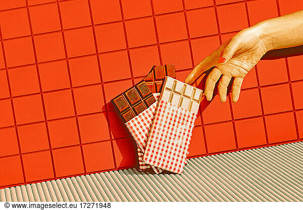 Mid adult woman hand choosing chocolate kept in line against red tile wall