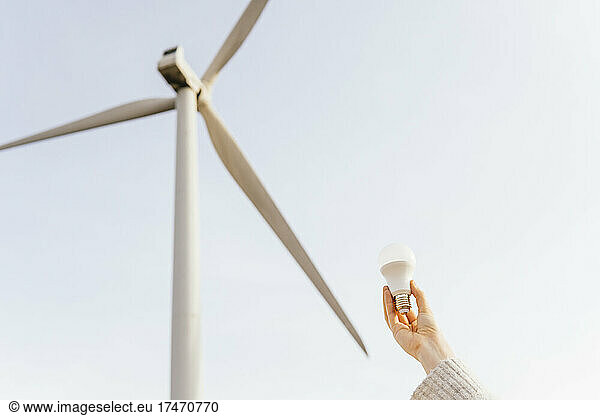 Mid adult woman holding light bulb at wind turbine