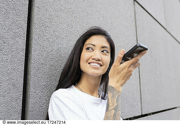 Mid adult woman holding smart phone by wall