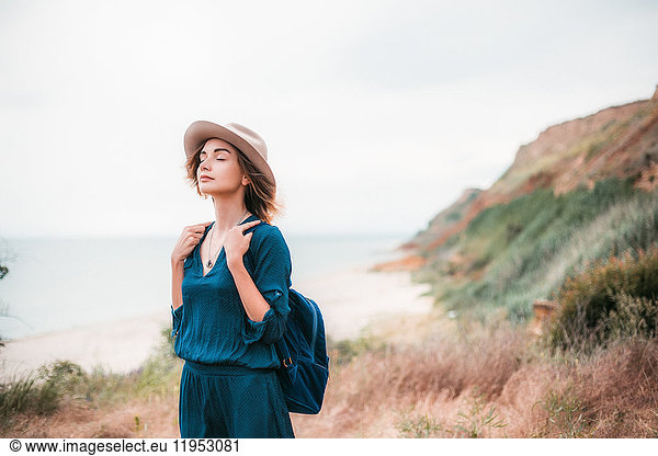 Mid adult woman in coastal setting  carrying backpack  breathing in fresh air