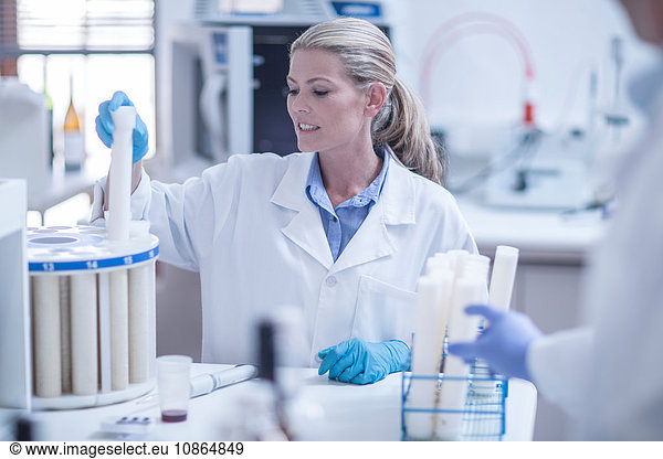 Mid adult woman in laboratory inserting test tube into tray
