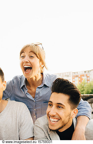 Mid adult woman laughing while standing by male friends at social gathering