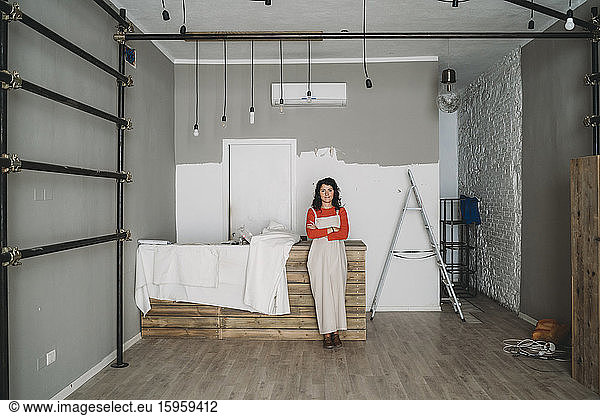 Mid adult woman leaning against table in her new shop  full length portrait