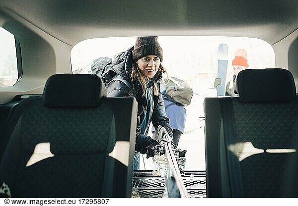 Mid adult woman loading skis in car trunk