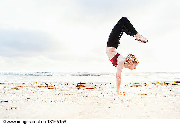 Mid adult woman practicing handstand yoga position on beach