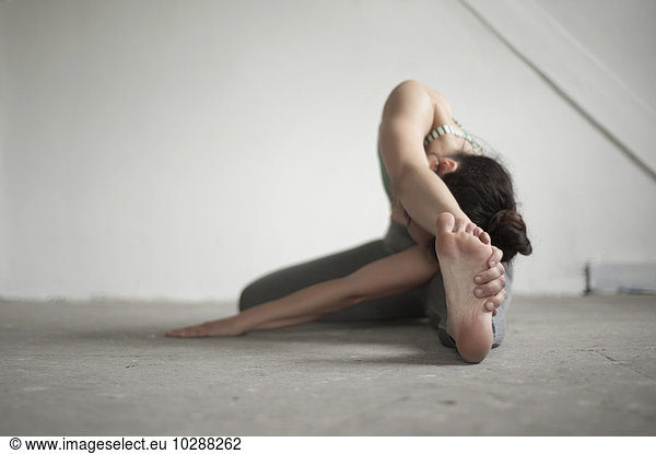 Mid adult woman practicing janu sirsasana pose in yoga studio  Munich  Bavaria  Germany