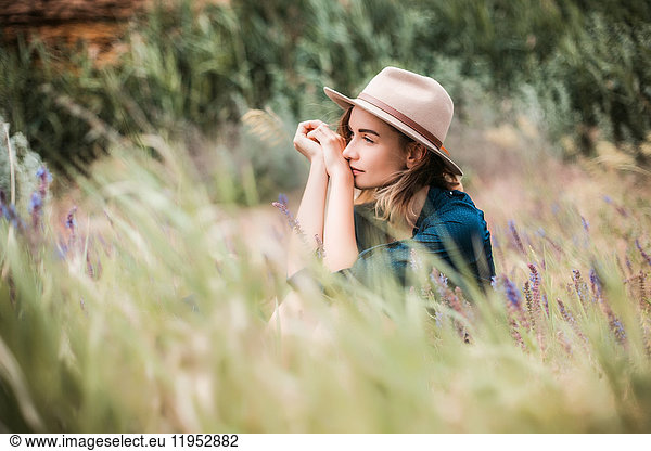 Mid adult woman sitting in long grass  thoughtful expressions