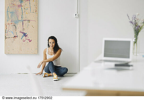 Mid adult woman sitting on floor against wall in loft at home