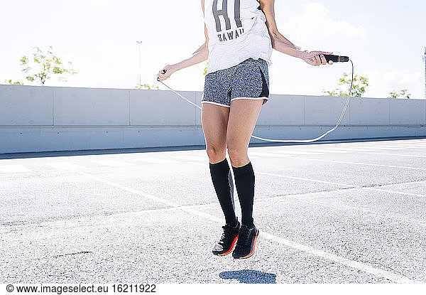 Mid adult woman skipping on road in city during sunny day