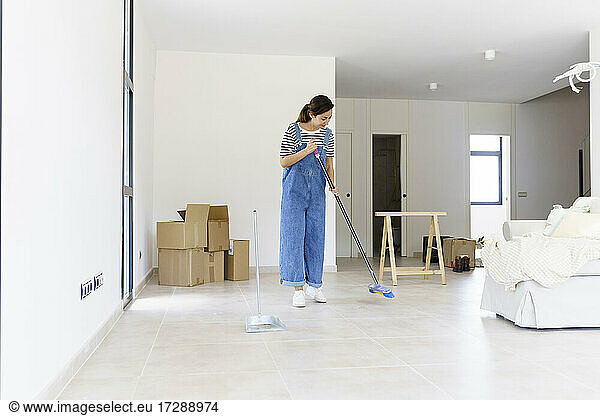 Mid adult woman sweeping living room floor at new home