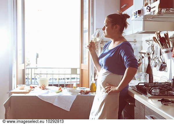 Mid adult woman taking a cooking break and drinking white wine in kitchen