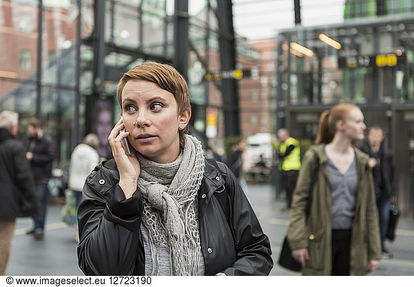 Mid adult woman talking on mobile phone with friend in background at station