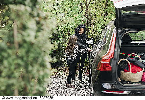 Mid adult woman teaching daughter to charge electric car at charging station