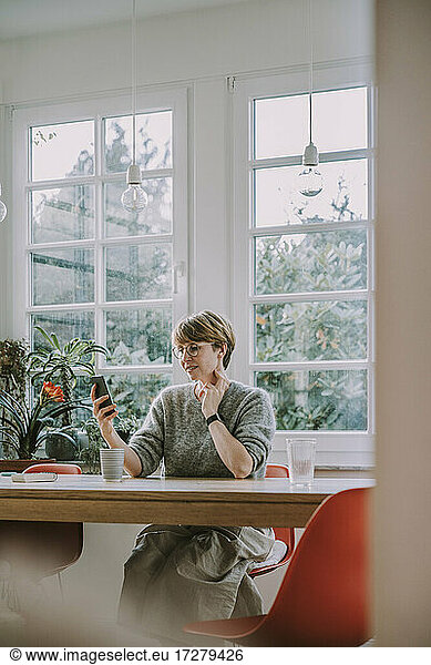Mid adult woman text messaging on smart phone at home
