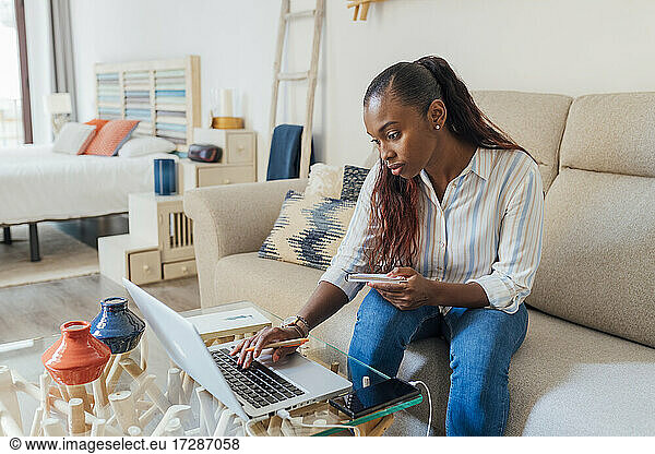 Mid adult woman using laptop while sitting with note pad at home