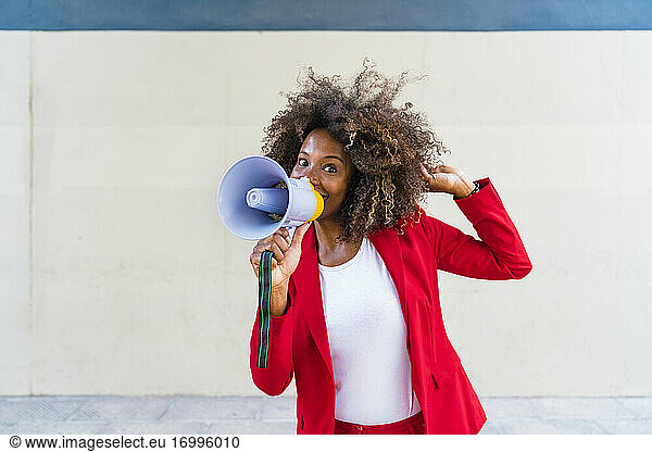 Mid adult woman using megaphone while standing against wall