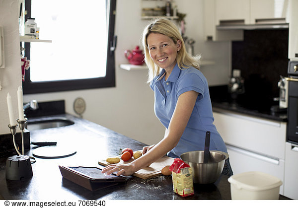 Mid adult woman using recipe on digital table and making meal in kitchen