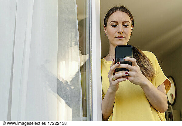 Mid adult woman using smart phone while leaning on window