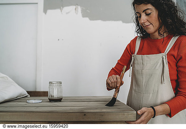 Mid adult woman varnishing wooden table in her new shop