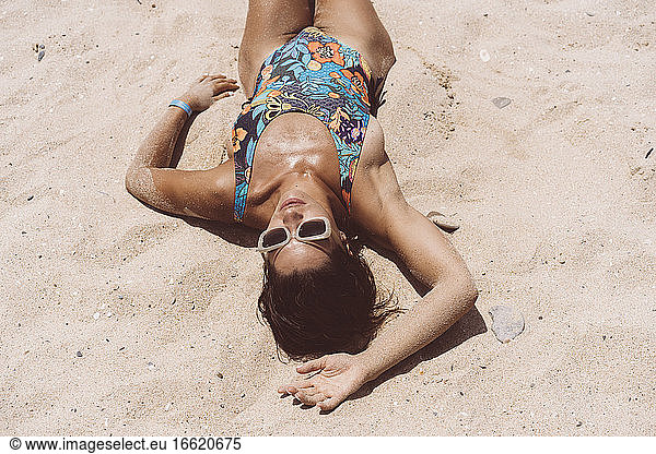 Mid adult woman wearing bodysuit lying at Valdevaqueros beach on sunny day  Tarifa  Spanien