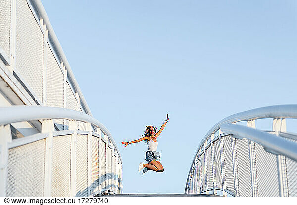 Mid adult woman with arms outstretched enjoying while jumping against clear sky