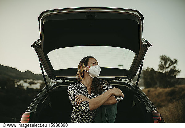 Mid adult woman with protective mask sitting at boot and looking sideways
