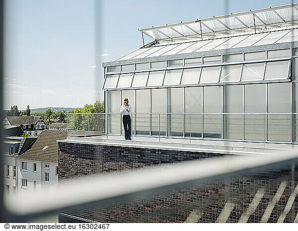 Mid distance view of businesswoman standing in balcony at greenhouse seen through window