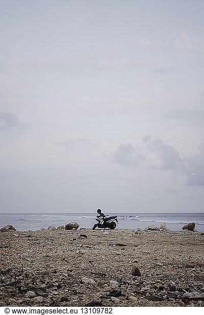 Mid distance view of motor scooter parked at beach against sky
