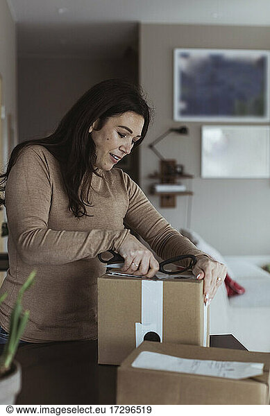 Mid erwachsene Frau Auspacken Box mit Schere zu Hause
