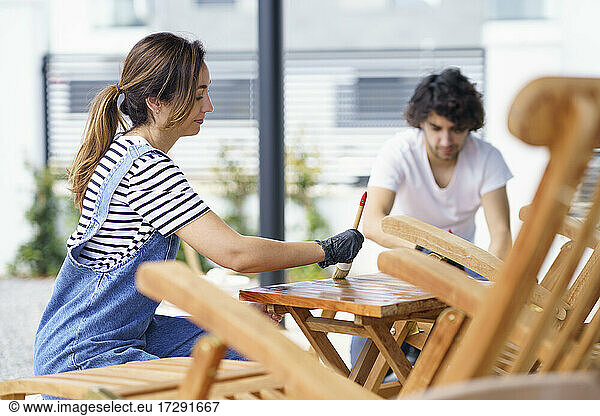 Mid erwachsene Frau poliert Holztisch während Freund im Hintergrund