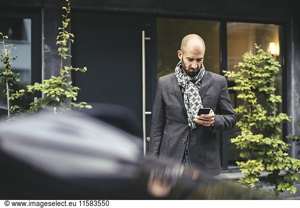 Mid Erwachsenen Geschäftsmann mit Smartphone gegen Gebäude