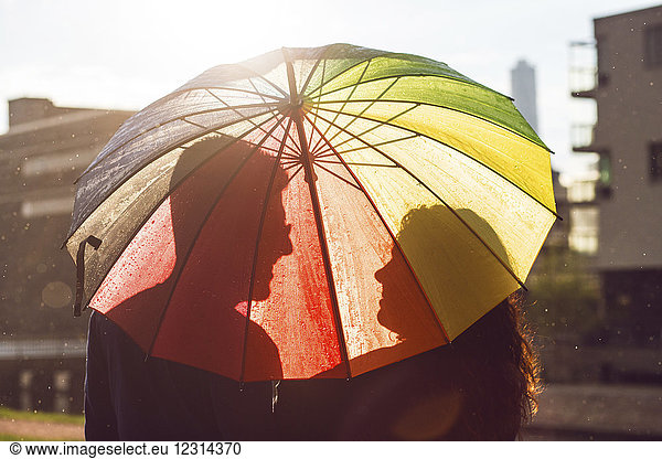 Mid erwachsenen Paar unter bunten Regenschirm bei Sonnenuntergang stehen