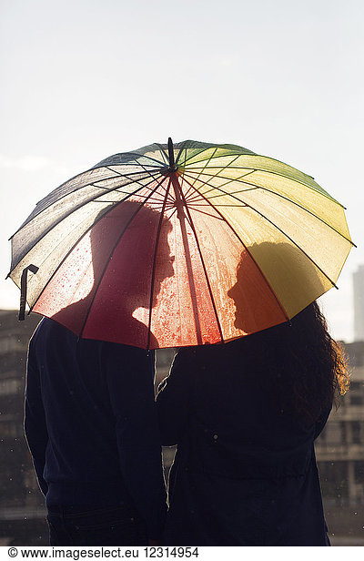 Mid erwachsenen Paar unter bunten Regenschirm bei Sonnenuntergang stehen