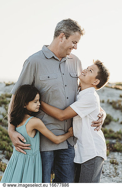 Mid-40's dad in gray shirt hugging preteen son and young daughter