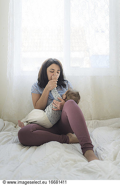 Mid-30's mom with closed eyes kissing hand of baby while breastfeeding