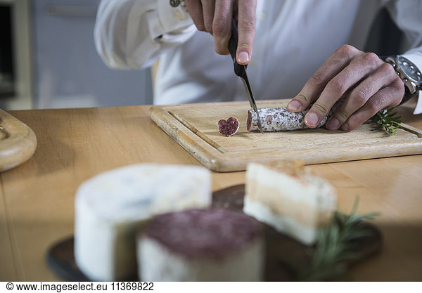 Mid section of a man cutting salami in the kitchen