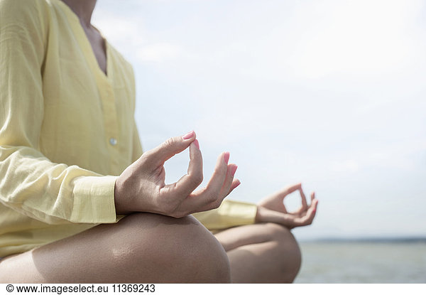 Mid section of a woman doing lotus pose yoga at the lake  Ammersee  Upper Bavaria  Germany