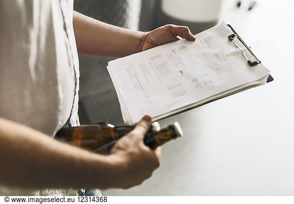 Mid section of brewery worker holding documents and beer
