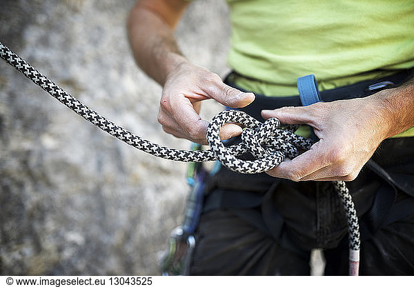 Mid section of man adjusting climbing rope
