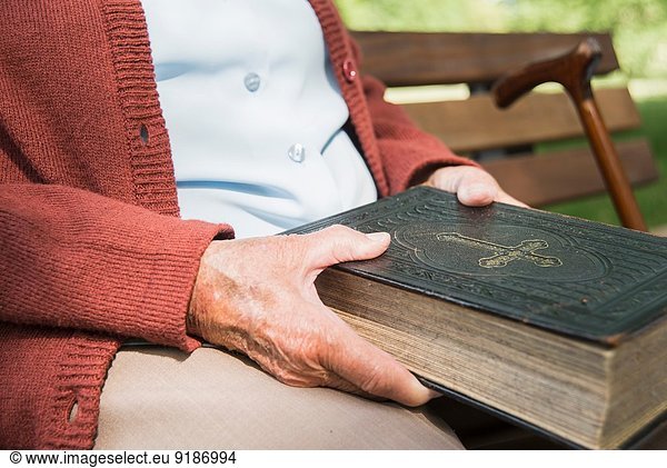 Mid section of senior woman  sitting on park bench  holding bible