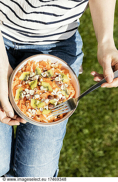 Mid section of woman eating bowl of fruit salad