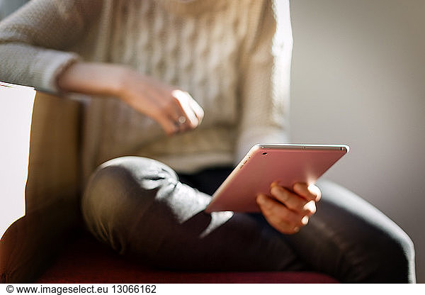 Mid section of woman holding tablet computer at home