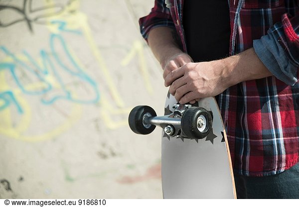Mid section of young man holding skateboard