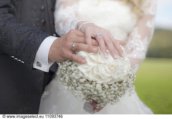 Mid section view of a bride and groom holding bouquet and showing their wedding ring