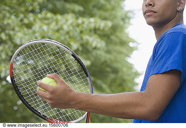 Mid section view of a teenage boy holding a tennis racket and a tennis ball