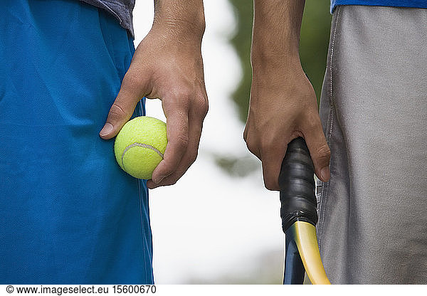 Mid section view of two teenage boys holding tennis ball and a tennis racket