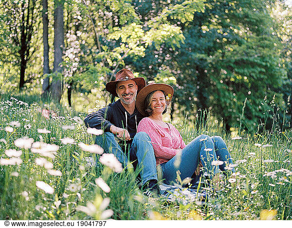 middle aged couple sitting together in the grass among wildflowers