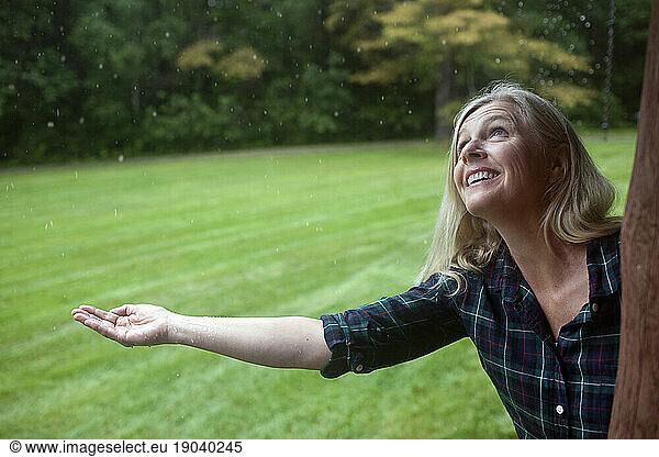 Middle-aged healthy woman expectantly reaches out for rain drops outside her cabin  in Kezar Lake  Maine