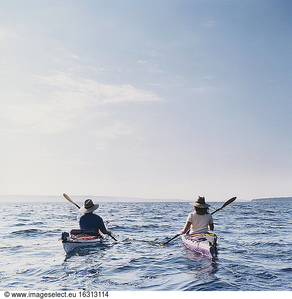 Middle aged man and woman sea kayaking on calm waters