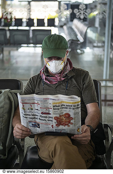 Middle aged man reads about Covid-19 while waiting at a deserted airport in Khajuraho  Madhya Pradesh  India  wearing a face mask to stay protected.
